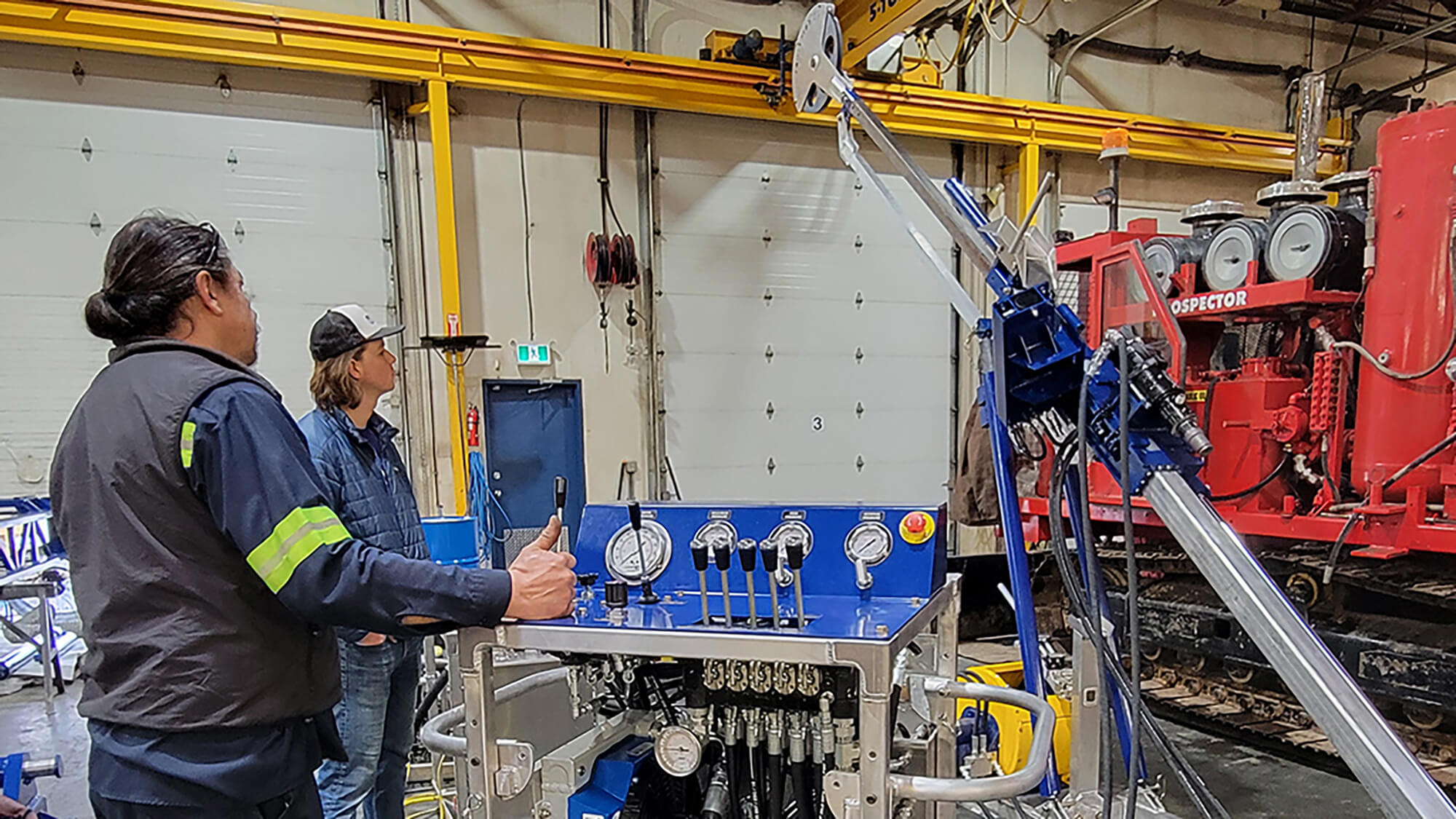A Multi-Power Products Ltd employee (foreground) demonstrates the BASE Drill to IDP engineer/driller Elliot Moravec (background). Credit: Jay Johnson.